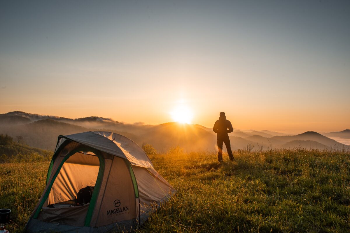 person watching the sunset by a tent